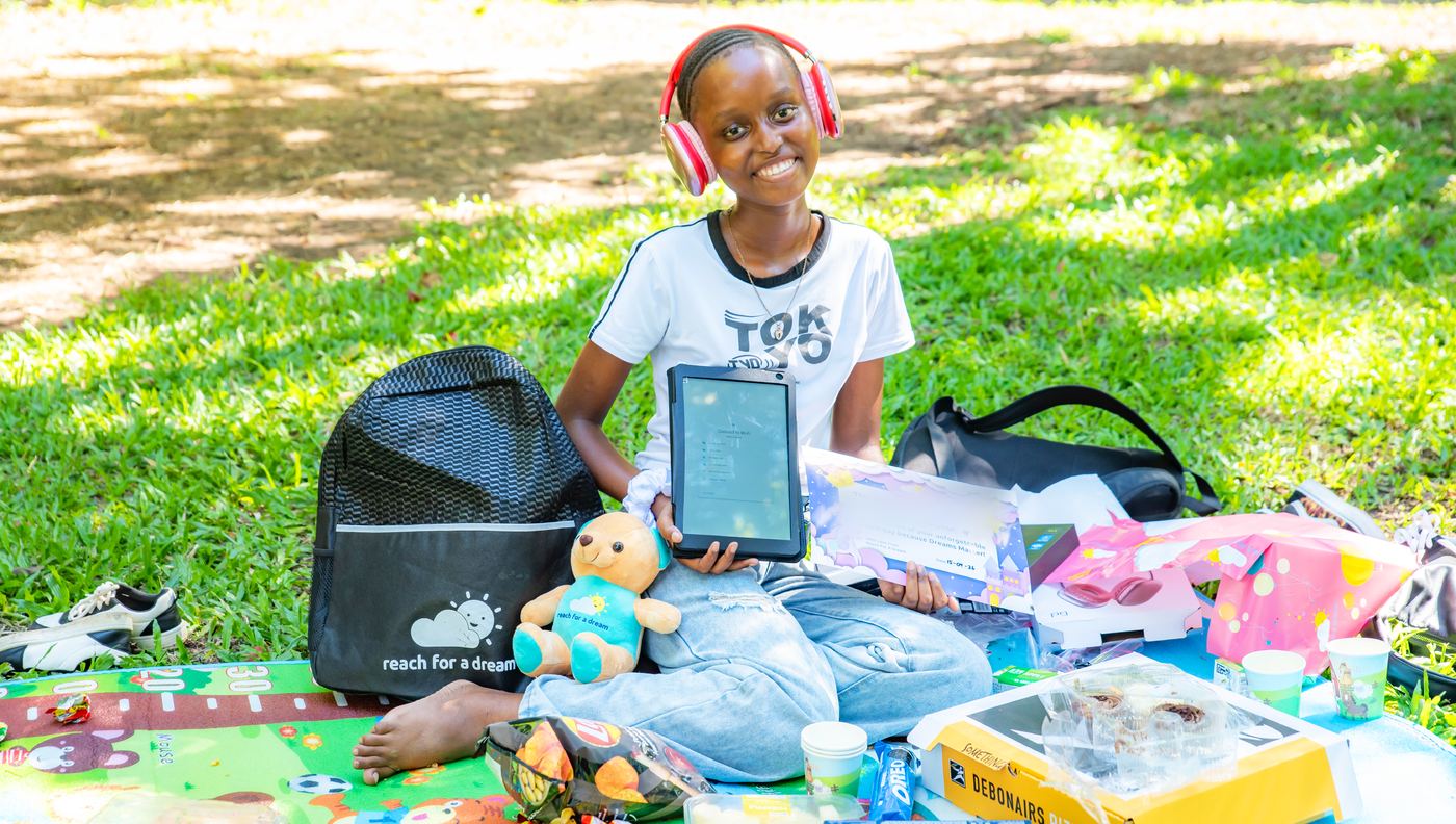 A girl seated on a picnic blanket in a park, holding a new tablet