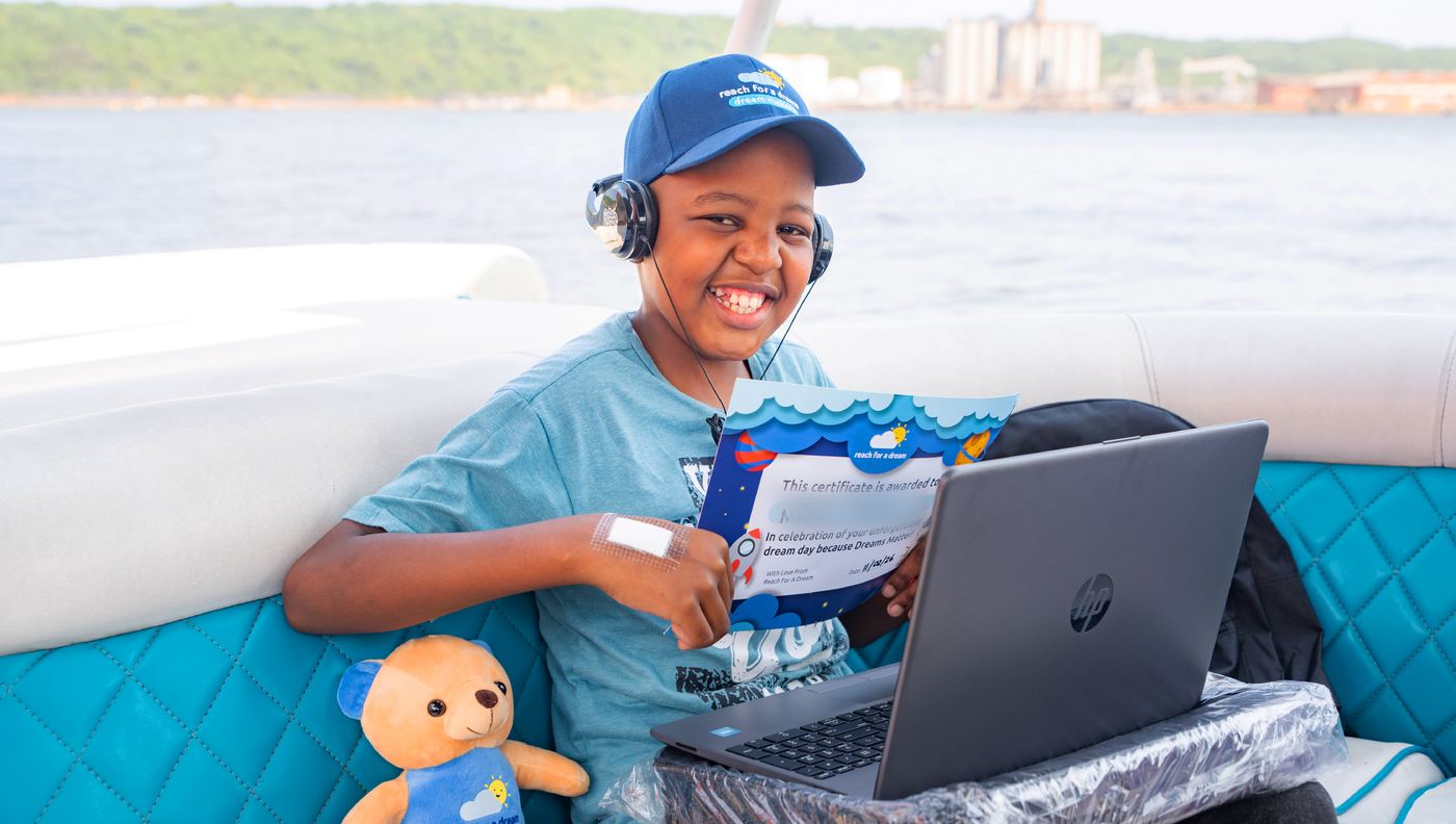 A boy on a boat on the bay, grinning behind a new laptop