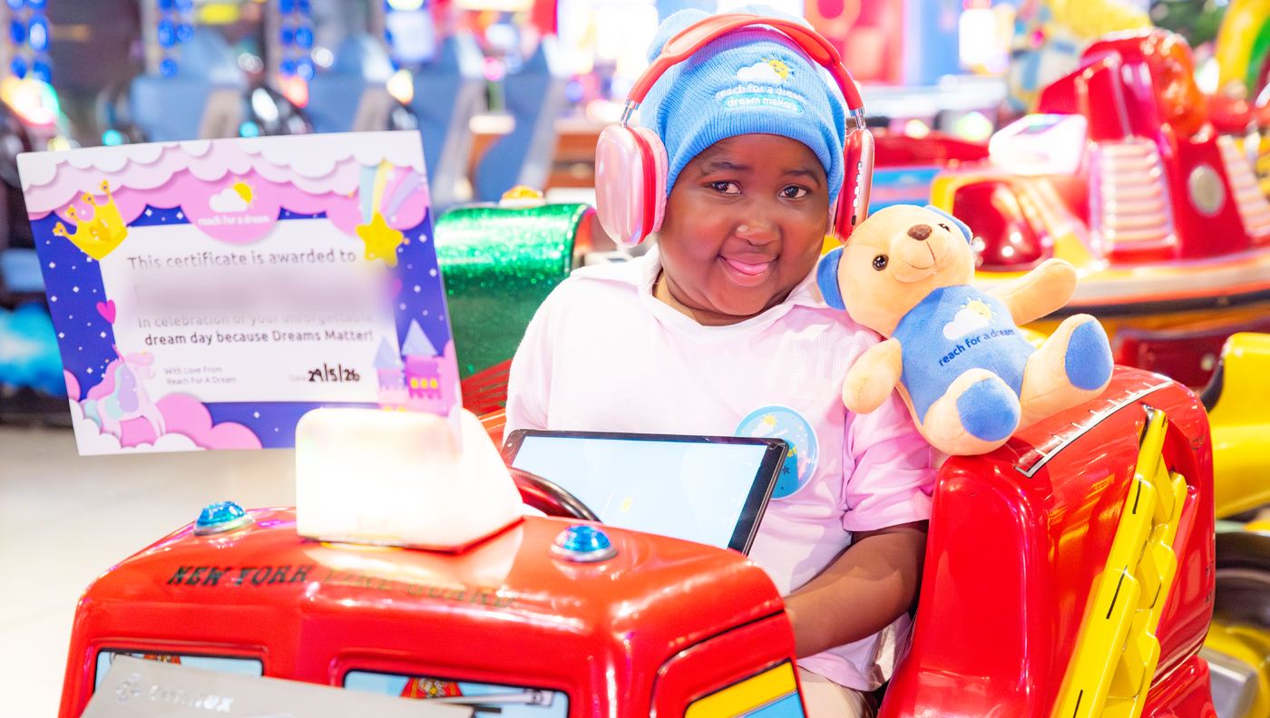 A girl in a ride-on fire engine holding a teddy bear, wearing headphones