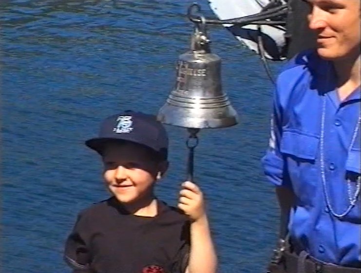 Chris as a boy ringing a ship bell beside a naval officer